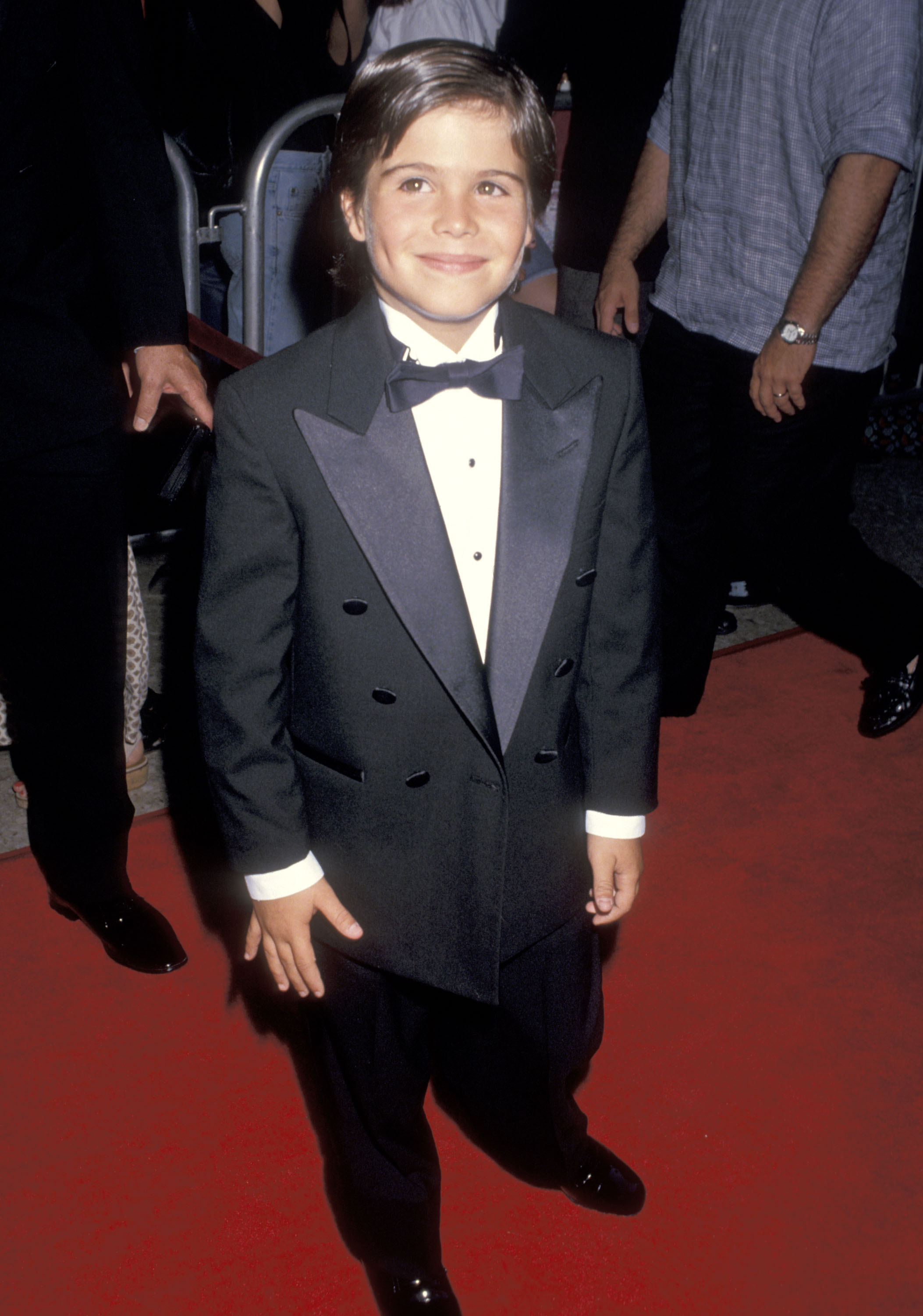 Ross Malinger smiles on the red carpet in a black tuxedo and bow tie at the Sleepless in Seattle premiere, enjoying one of the biggest moments of his childhood acting career. | Source: Getty Images.