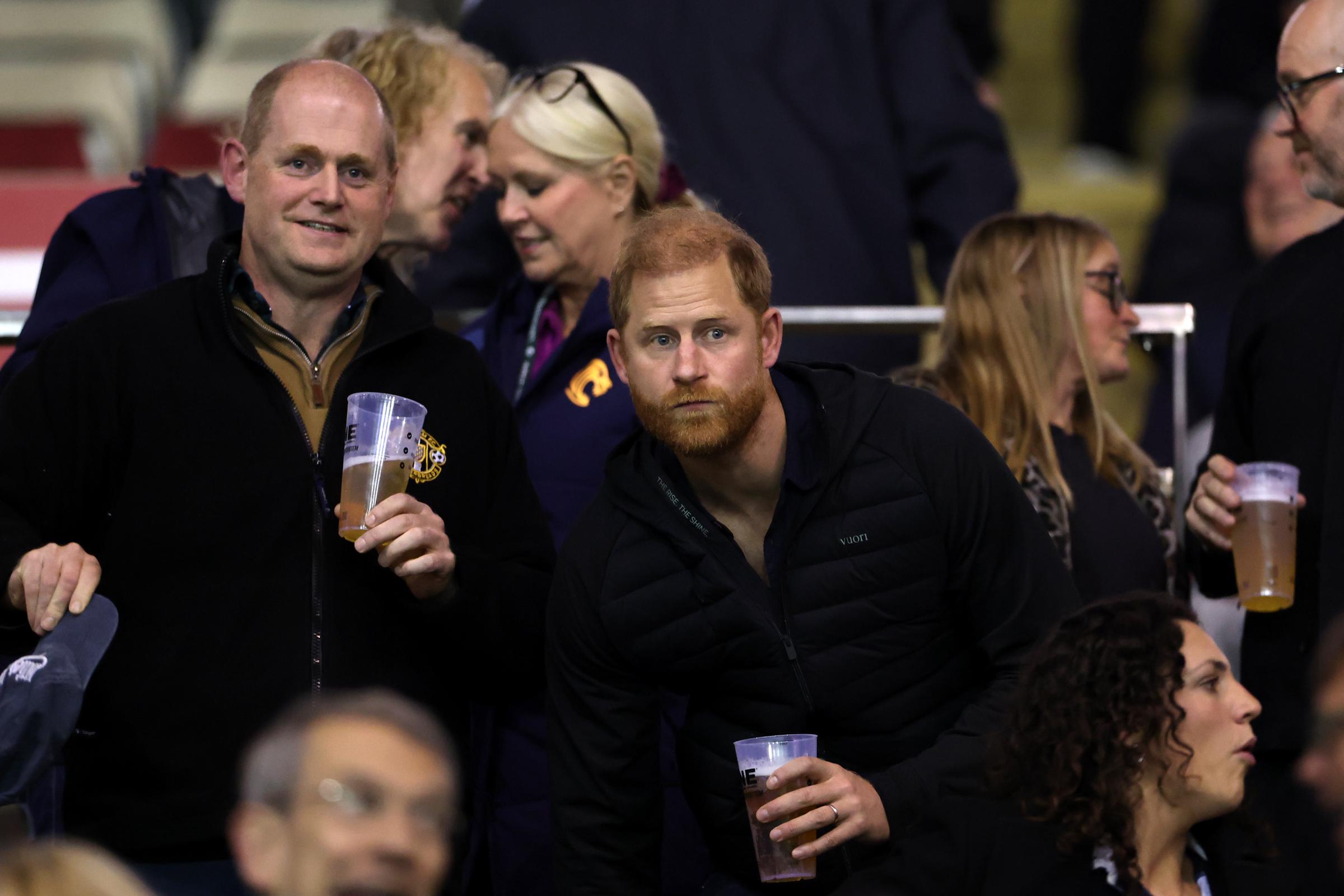 Prince Harry watches Leicester Tigers take on Gloucester Rugby at Mattioli Woods Welford Road Stadium on October 9, 2026, in Leicester, England. Wearing a black puffer jacket, he holds a drink and gestures while following the action. | Source: Getty Images
