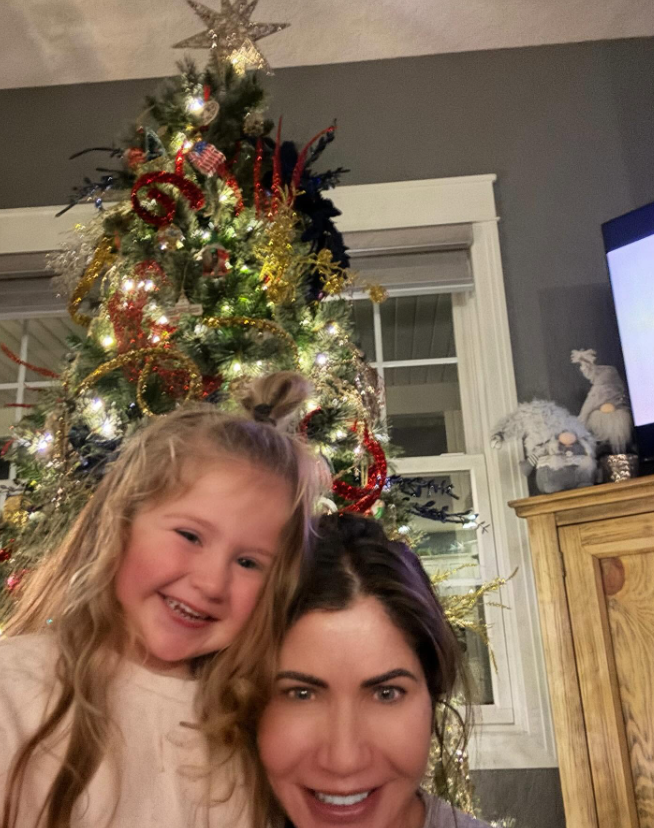 Another Christmas photo shows a more casual side of the living space. A decorated tree stands beside a window, while a large wooden cabinet and television are visible nearby. | Source: Facebook/kristi.noem